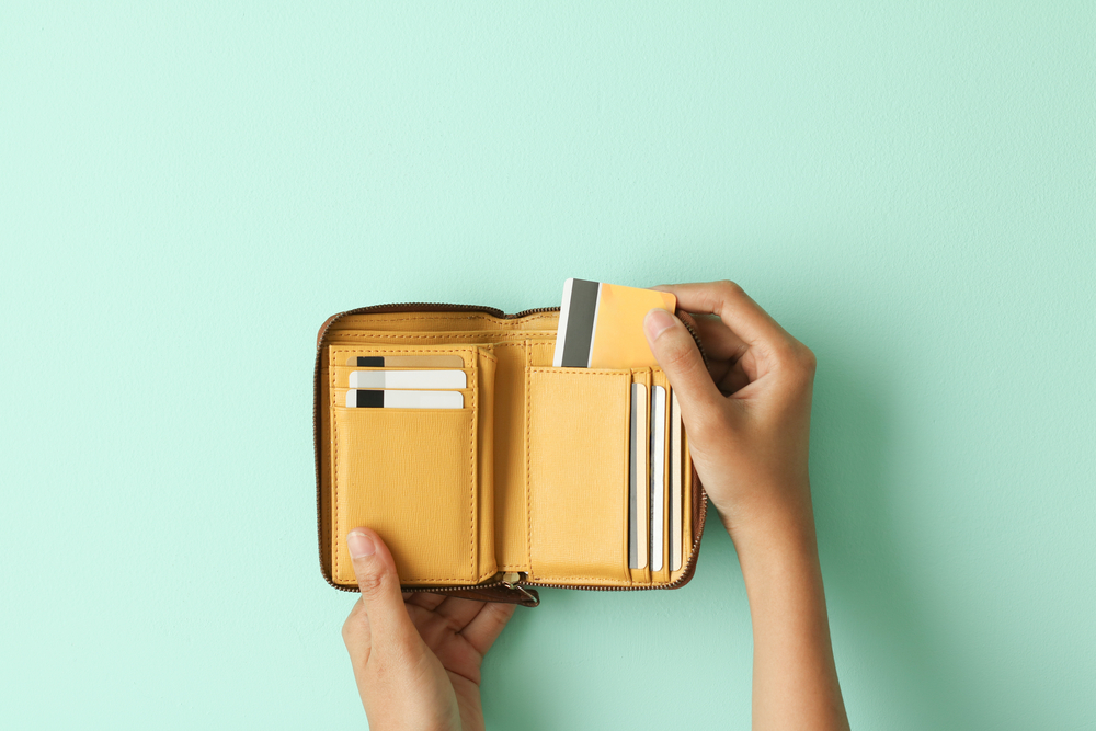 a hand holding a yellow wallet with a credit card